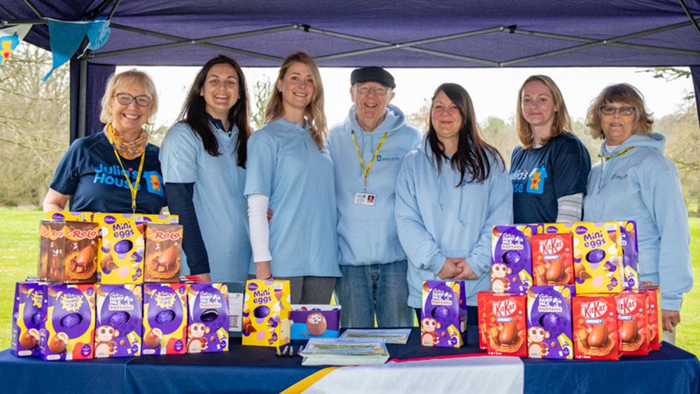 A group of Julia's House volunteers of all ages posing behind Easter Eggs that they gave out at our Easter Trail