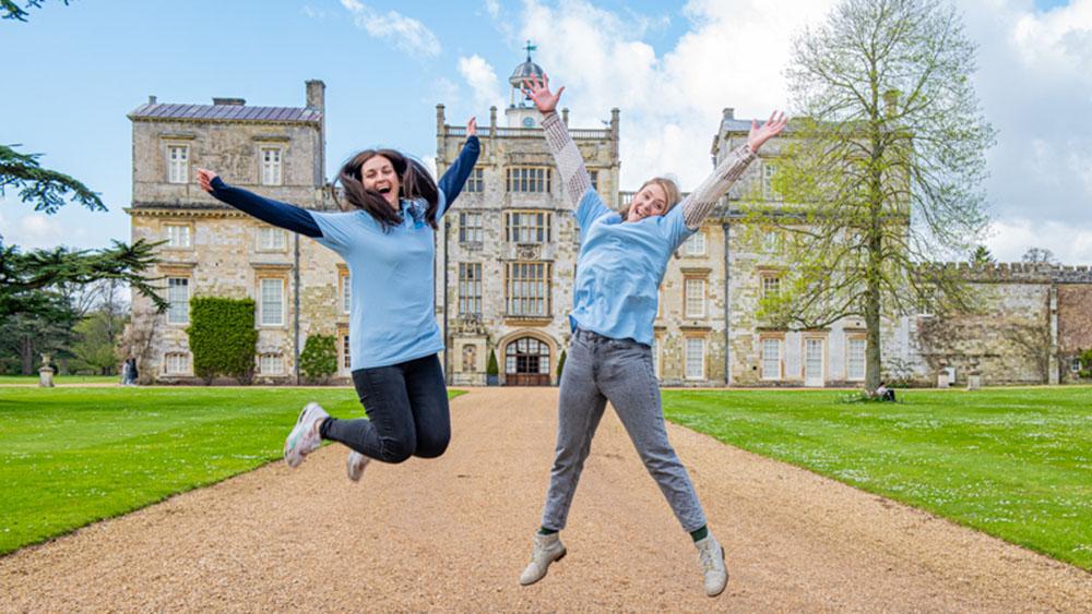 Two Julia's House volunteers jumping with arms in the air outside our Easter Egg trail venue Wilton House