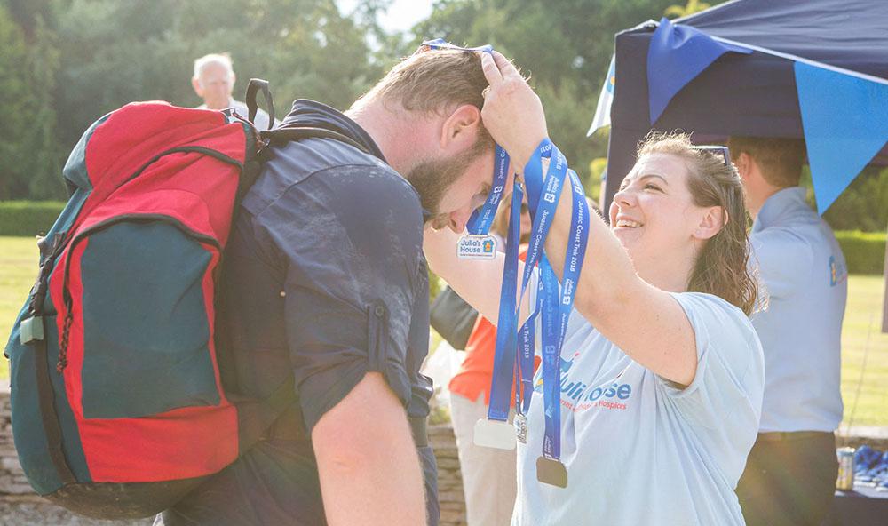 Julia's House volunteer placing medal round the neck of someone who has just finished a charity trek