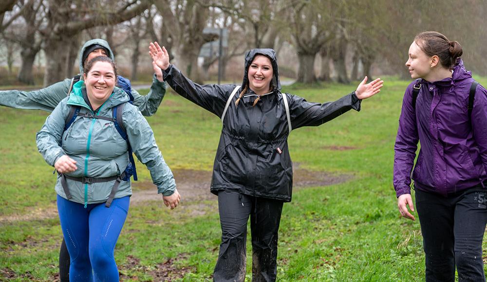 Diana and two other members of her team walking in a field in the rain with their hands up, smiling at the camera