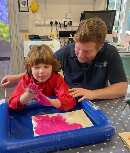 Ashley, helping one of the children Julia's House Children's Hospice support to make cards to send home. Olivia loves playing with paint so she is dipping her hands in paint and creating pink handprints.